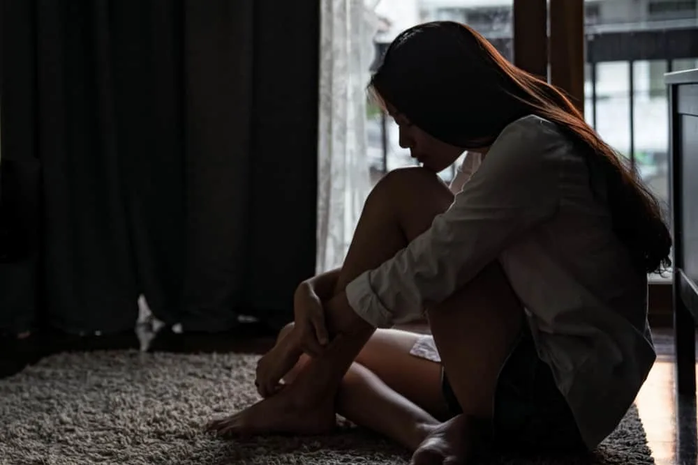 Eine traurige asiatische Frau sitzt auf dem Boden eines Raumes im Dunkeln