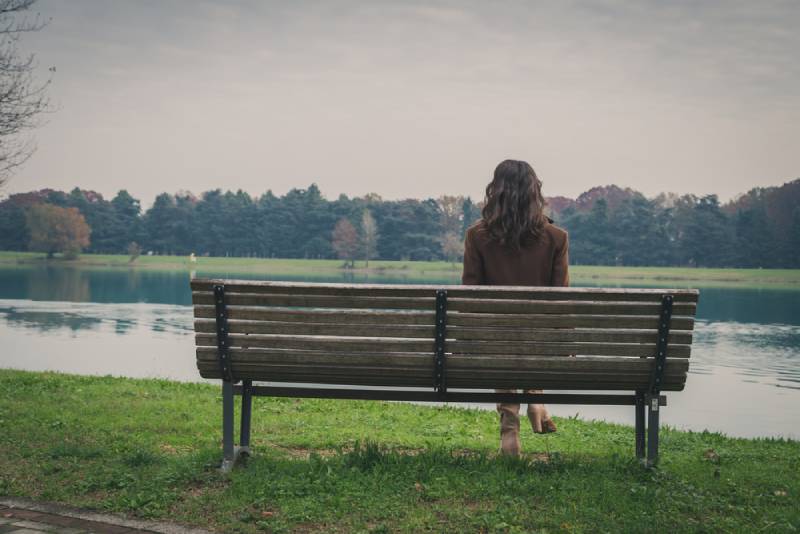 Schöne junge Frau mit langen Haaren, die auf einer Bank in einem Stadtpark sitzen