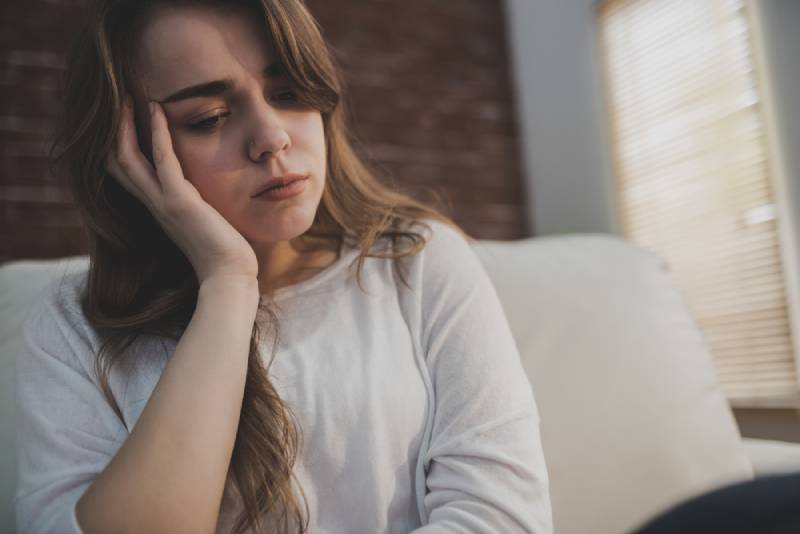 Wütende Frau, die auf der Couch sitzt und ihren Kopf im Wohnzimmer hält