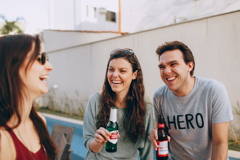 Ein lächelnder Mann und zwei Frauen trinken draußen Bier