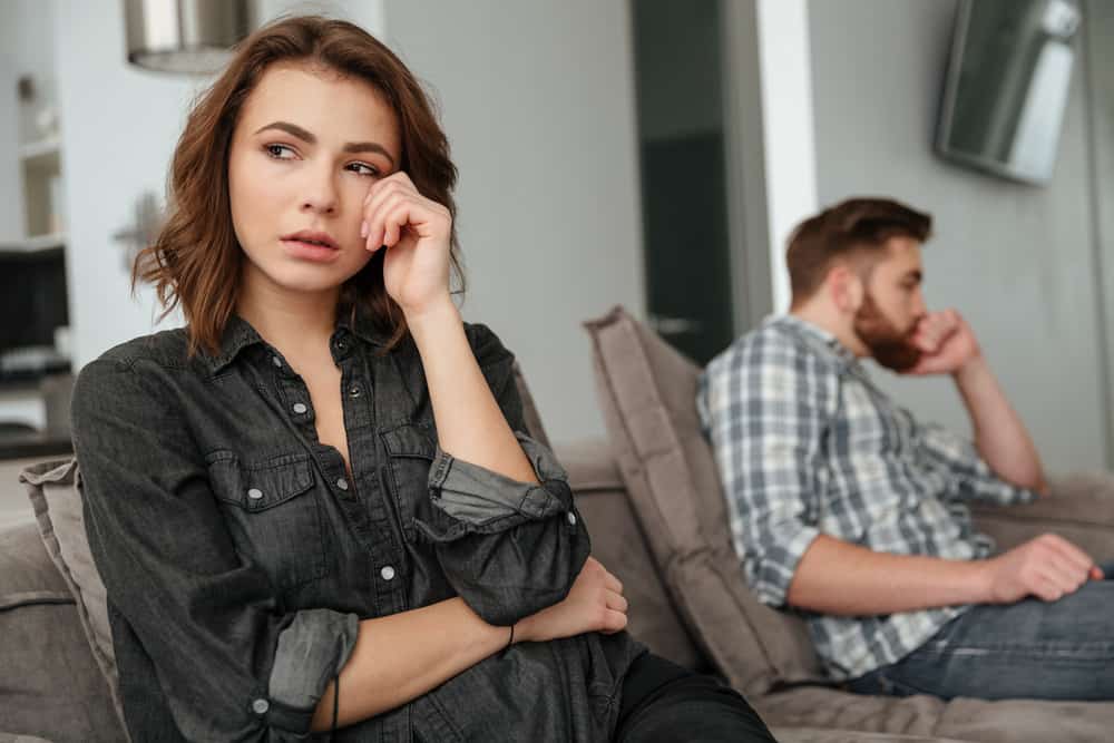 Eine traurige Frau sitzt und denkt neben ihrem desinteressierten Mann