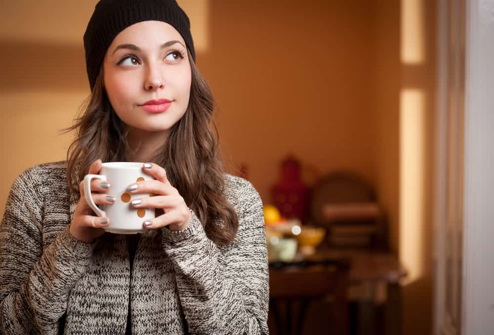Ein Mädchen mit einem Hut auf dem Kopf und einer Tasse Tee in den Händen denkt nach