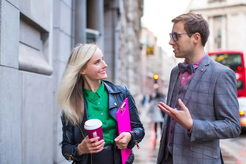 Ein Mann und eine Frau unterhalten sich auf der Straße, während sie Kaffee in der Hand hält
