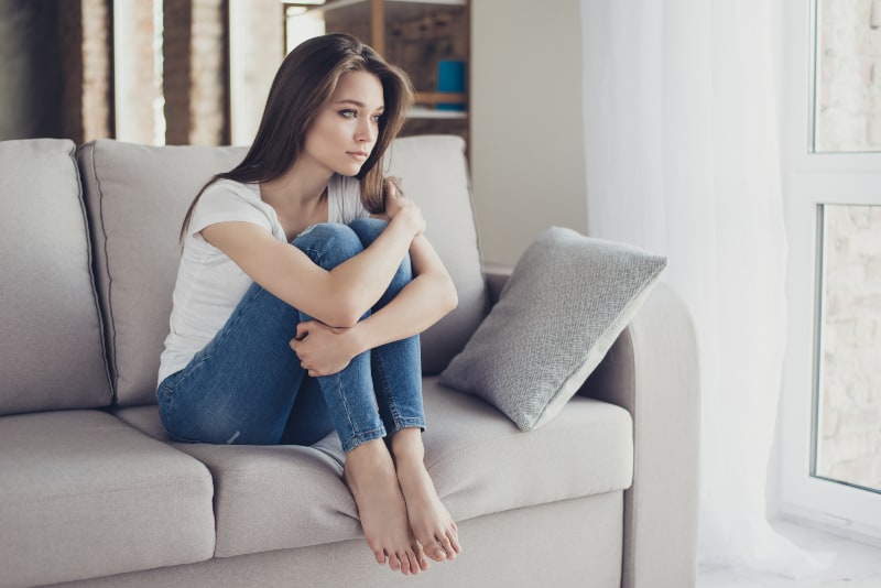 Ein junges schönes Mädchen sitzt auf der Couch und schaut traurig in die Ferne