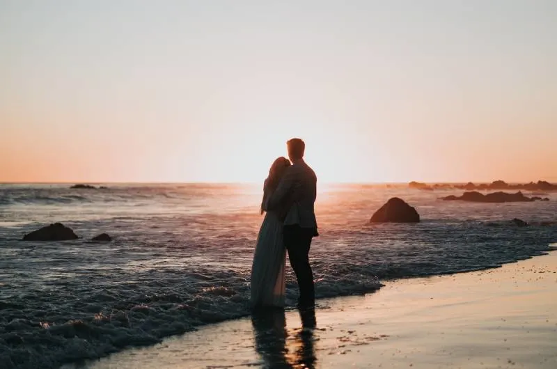 Schattenbildfoto des Paares, das am Strand steht und Sonnenuntergang beobachtet