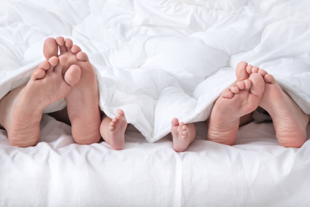 die Beine eines Mannes, einer Frau und eines Babys unter einer weißen Decke