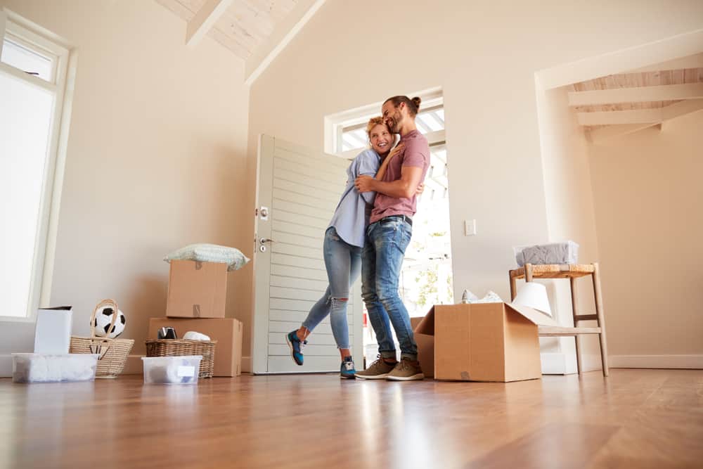 ein glückliches Paar, das in einer unmöblierten Wohnung mit Pappkartons steht