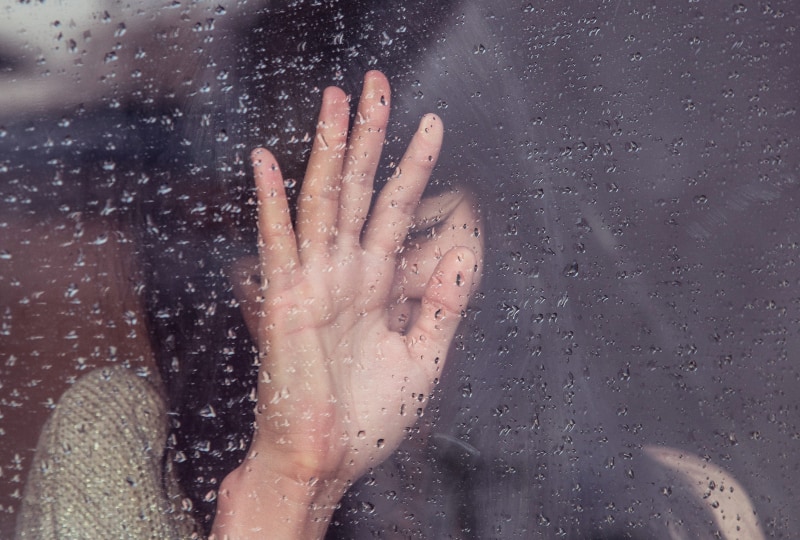 eine Frau berührt das Glas, auf dem es regnet