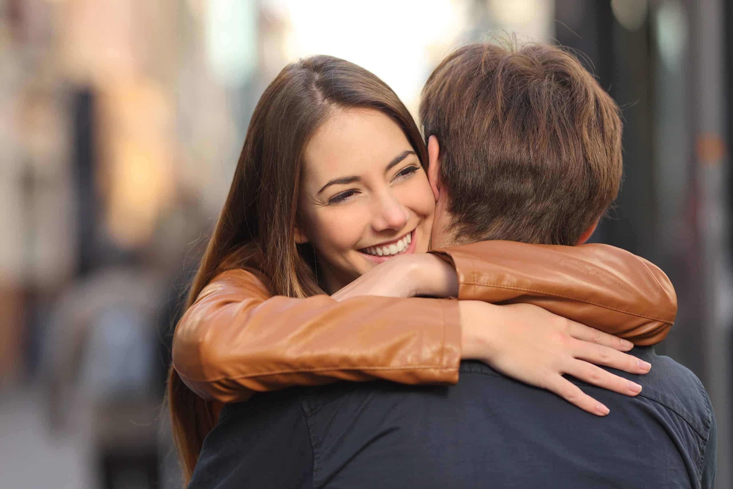 eine glückliche Frau mit einer braunen Jacke und ihrem Mann in einer Umarmung