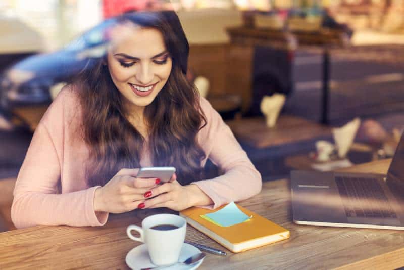 lächelnde Frau, die auf ihrem Telefon im Café tippt