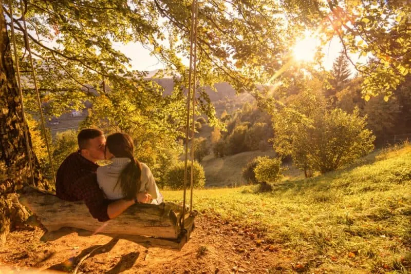 ein liebendes Paar auf einer Schaukel unter einem Baum küsst