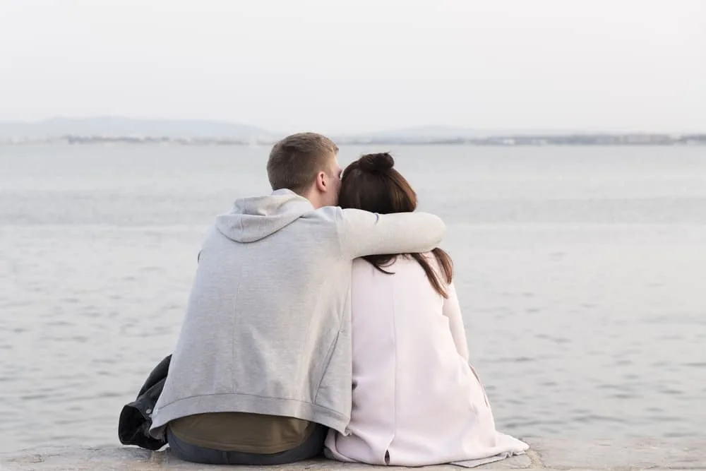 Ein Mann am Strand sitzt und umarmt seine Frau fest