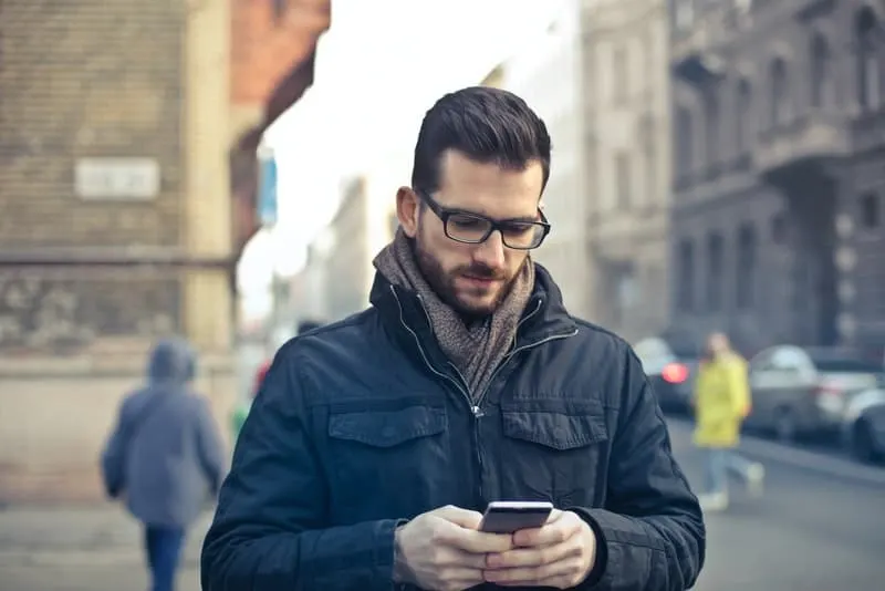 Ein Mann mit Brille und schwarzer Jacke schreibt eine Nachricht auf sein Handy