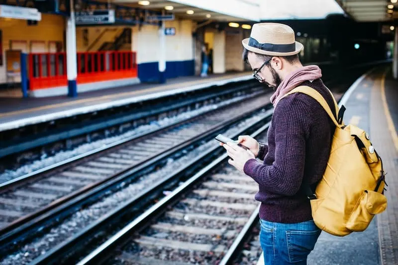 Ein Mann mit einem Hut auf dem Kopf an einem Bahnhof benutzt ein Handy