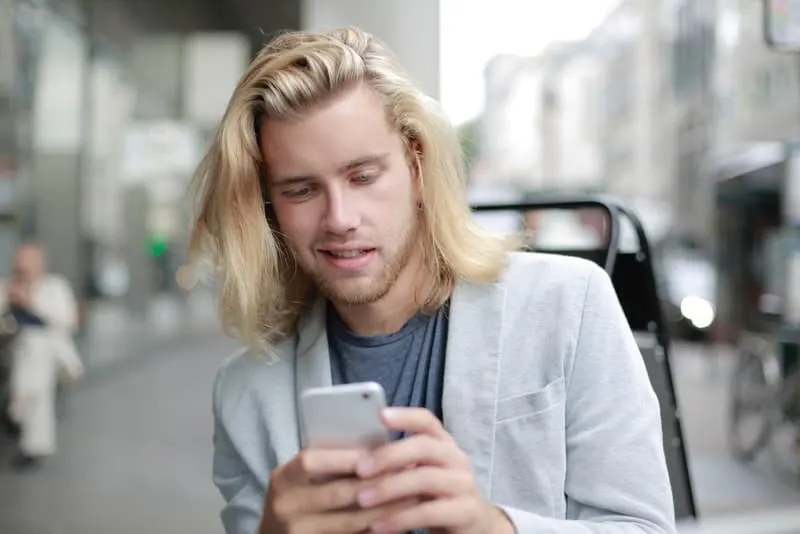Ein Mann mit langen blonden Haaren schreibt eine SMS