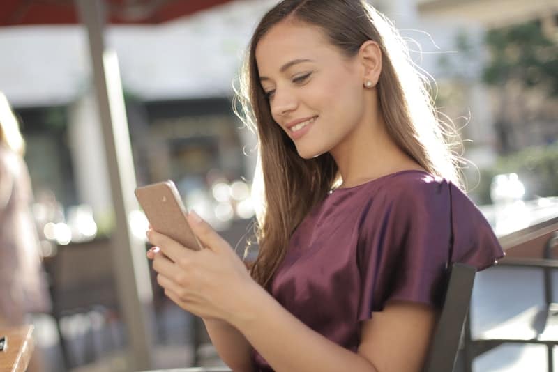Eine Frau in einem lila T-Shirt mit einem Lächeln liest den Inhalt auf ihrem Handy