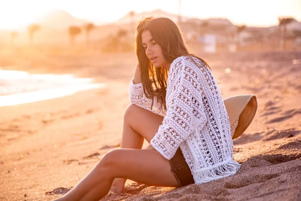 Eine traurige Frau in kurzen Hosen sitzt an einem Sandstrand