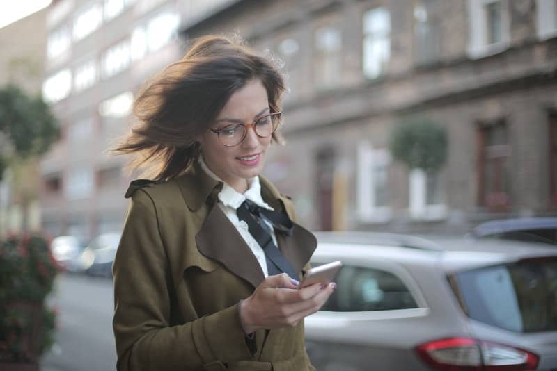 Eine zufriedene Frau in einem grünen Mantel liest eine Nachricht auf ihrem Handy