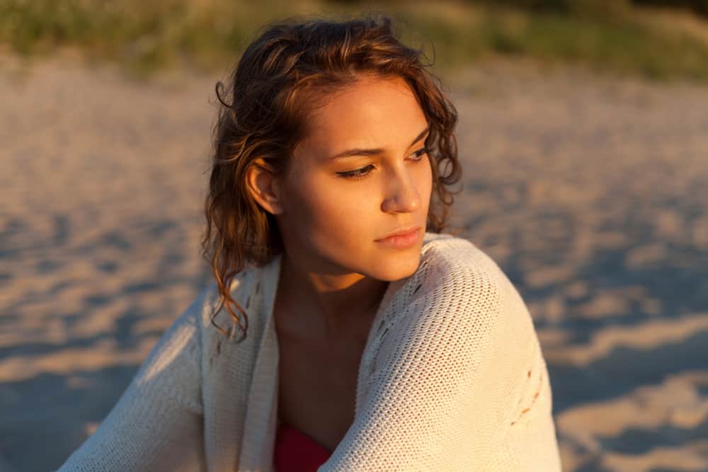 An einem Sandstrand sitzt eine traurige Frau in einem weißen Pullover
