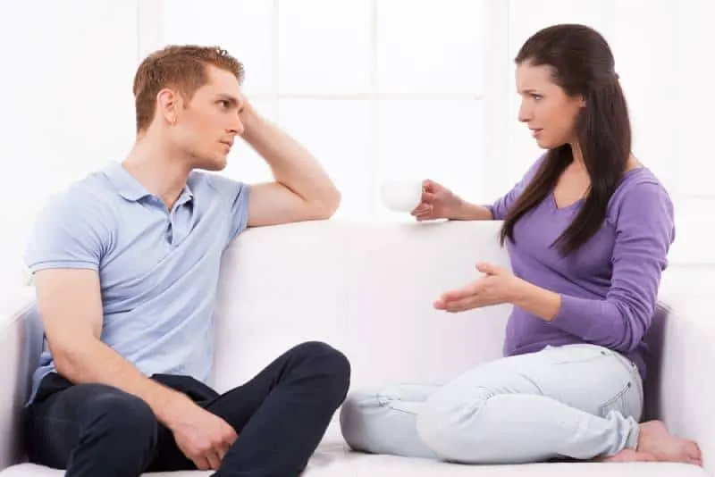 Deprimierter junger Mann, der auf der Couch sitzt und seine Freundin ansieht