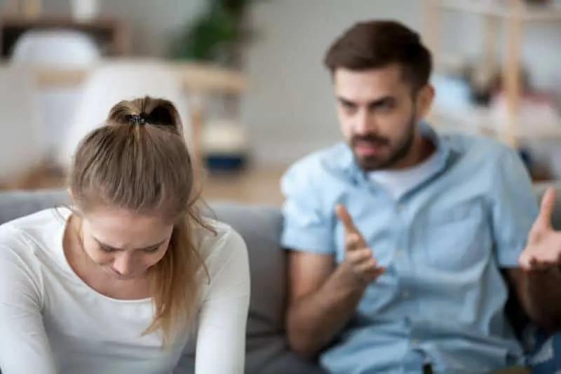 Verärgerte Frau sitzt weinend auf der Couch und hört dem wütenden Ehemann zu, der schreit