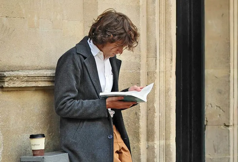 Draußen an der Wand gelehnt steht ein Mann und liest ein Buch