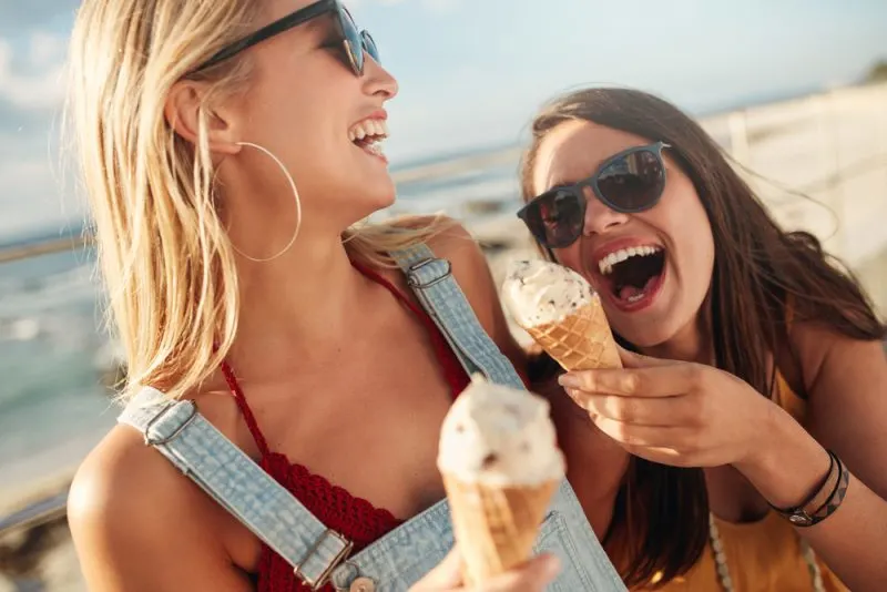 zwei lächelnde Freunde am Strand mit Eis in den Händen