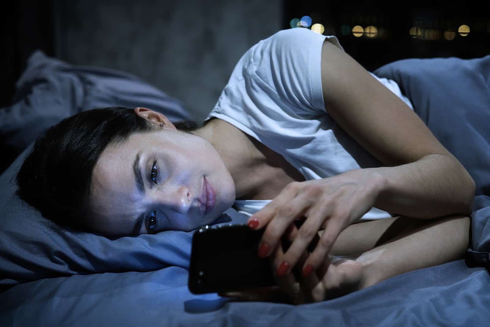 Frau, die in ihrem Bett liegt und jemandem eine SMS schreibt