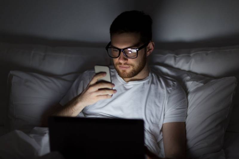 Mann mit Brille, der vor dem Schlafengehen auf seinem Telefon tippt