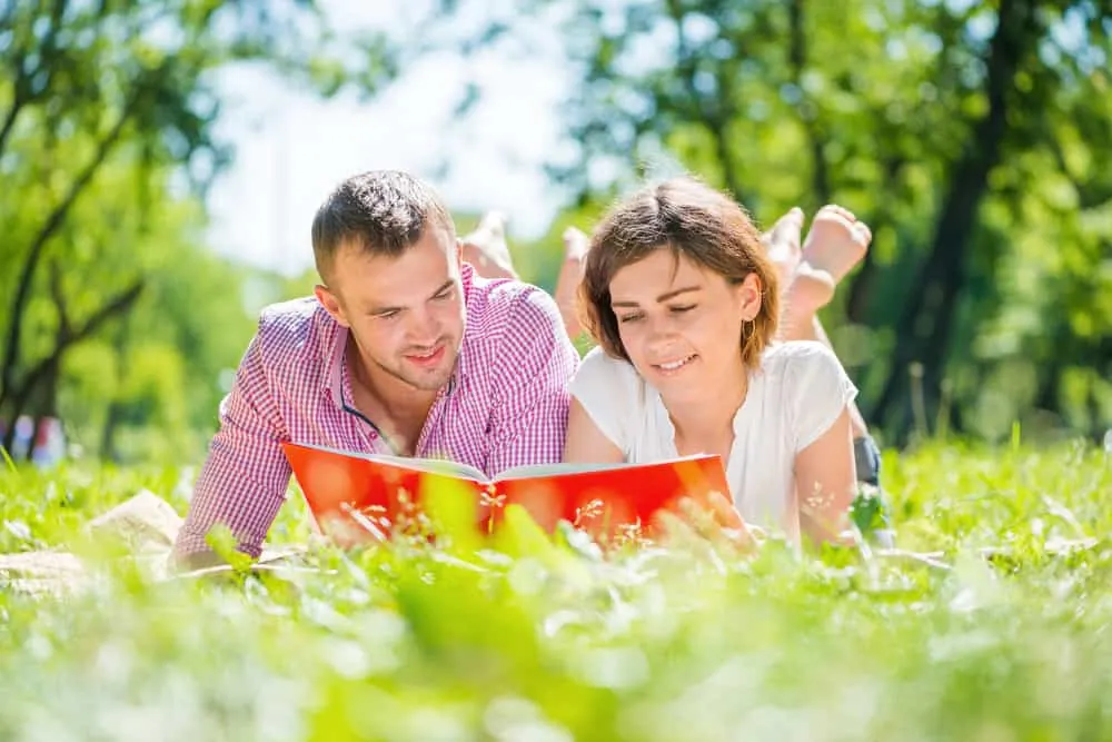 ein lächelndes Barfußpaar, das im Gras liegt und ein Buch liest