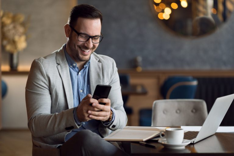 ein lächelnder Geschäftsmann, der in einem Café sitzt und SMS schreibt