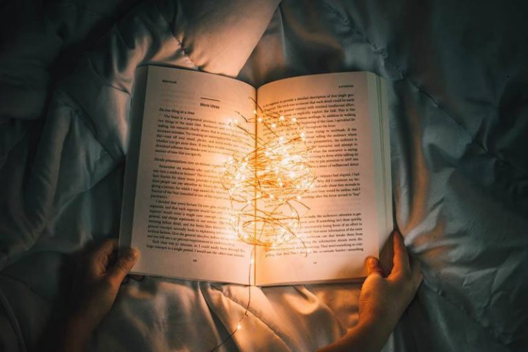 Hände halten ein offenes Buch auf dem Bett