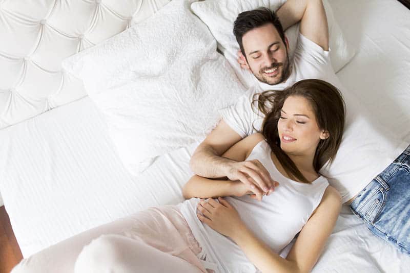 Der glückliche Mann und die glückliche Frau liegen im Bett und halten sich an den Händen