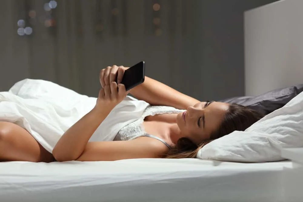 Die Frau liegt im Schlafzimmer und benutzt ein Handy