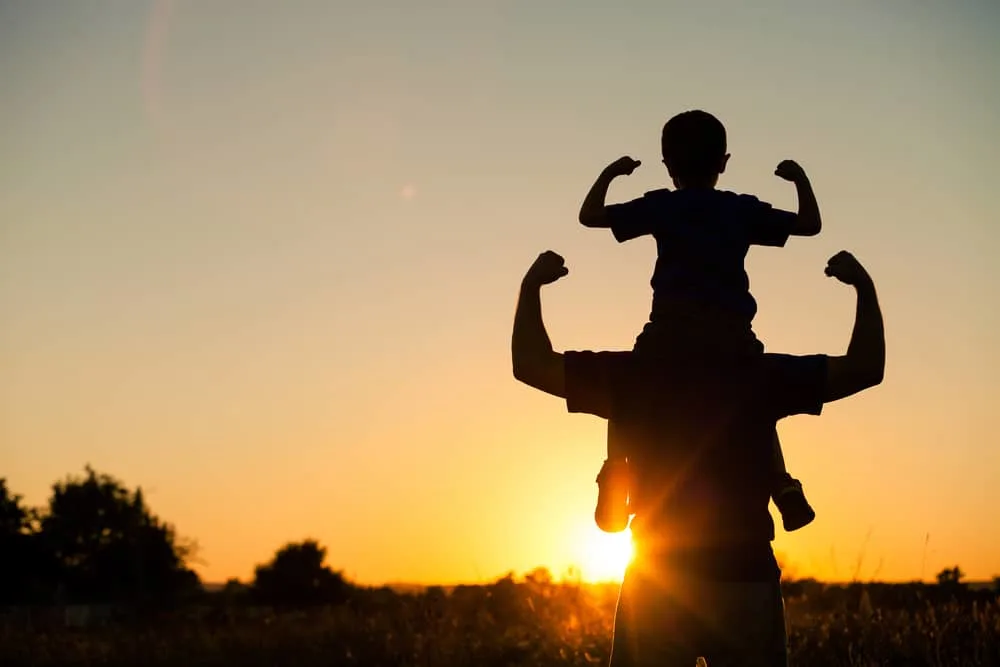 Ein Mann bei Sonnenuntergang hält seinen Sohn auf den Schultern
