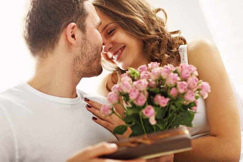 Ein Mann gibt einer lächelnden Frau einen Blumenstrauß und ein Geschenk