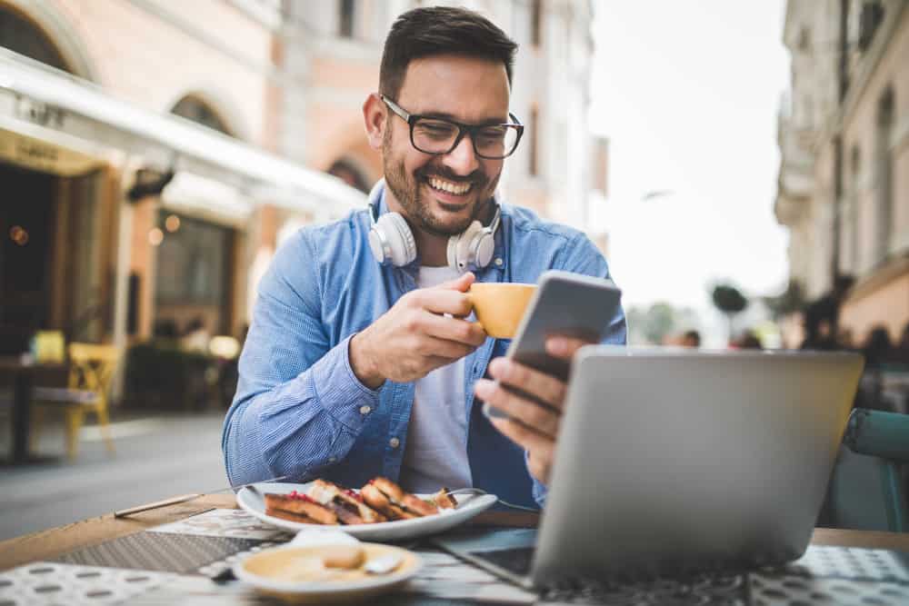 Ein lächelnder Mann mit einem Telefon in der Hand frühstückt auf der Restaurantterrasse