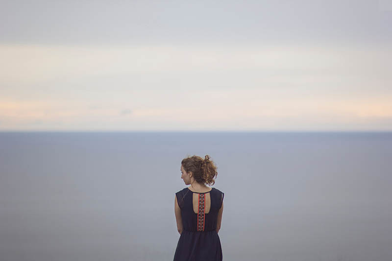 Eine Brünette in einem ungewöhnlichen Kleid steht am Meer