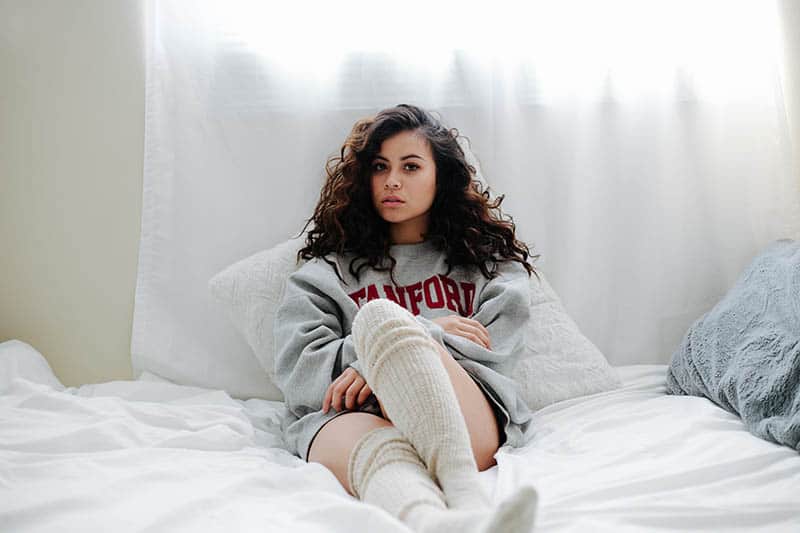 Eine attraktive Brünette in Sweatshirt und Socken sitzt auf einem Doppelbett