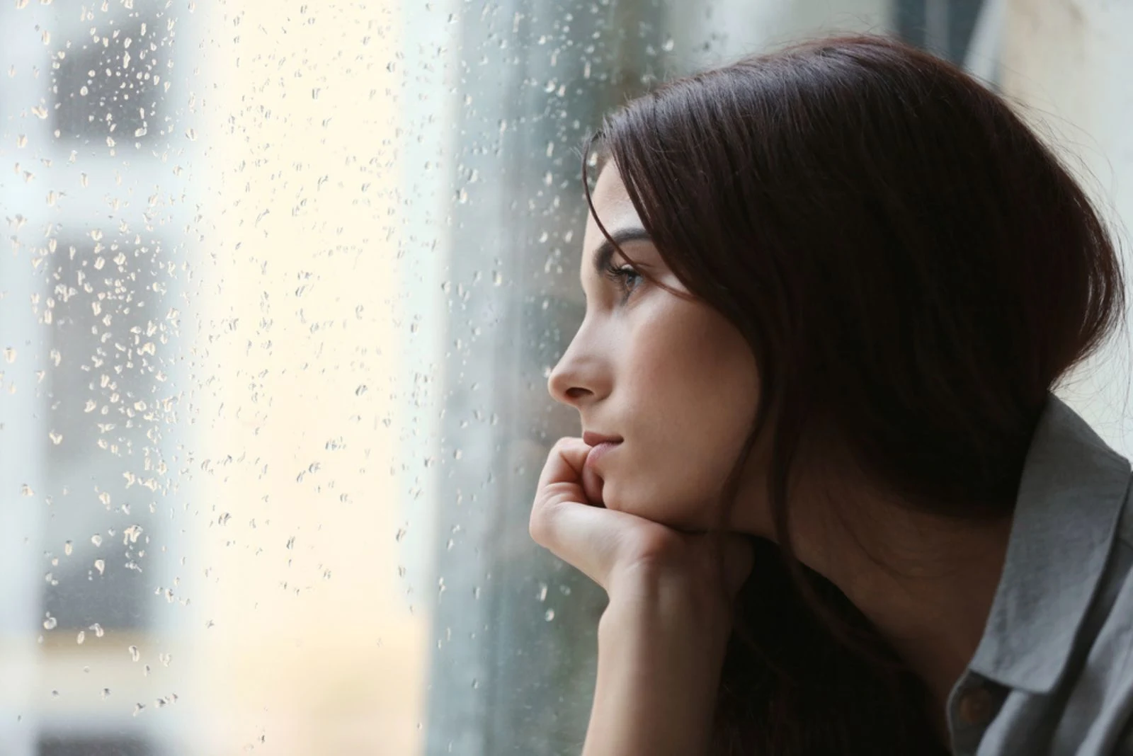 Traurige Frau schaut durch verregnetes Fenster