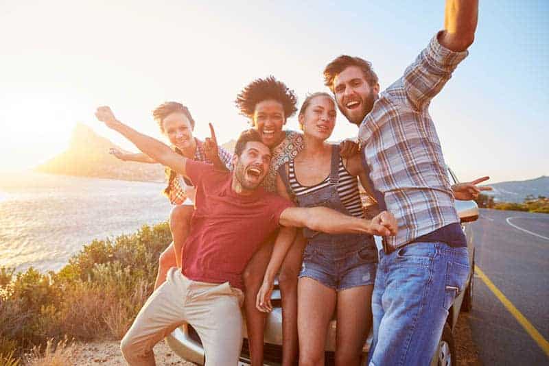 eine Gruppe glücklicher Freunde, die vor einem Auto an der Straße stehen