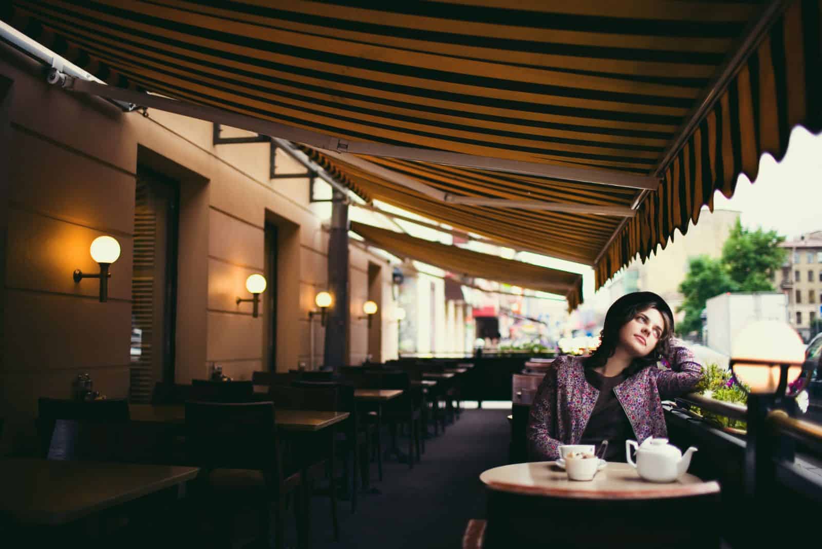 Ein imaginäres Mädchen mit Hut auf dem Kopf sitzt an einem Tisch in einem Café