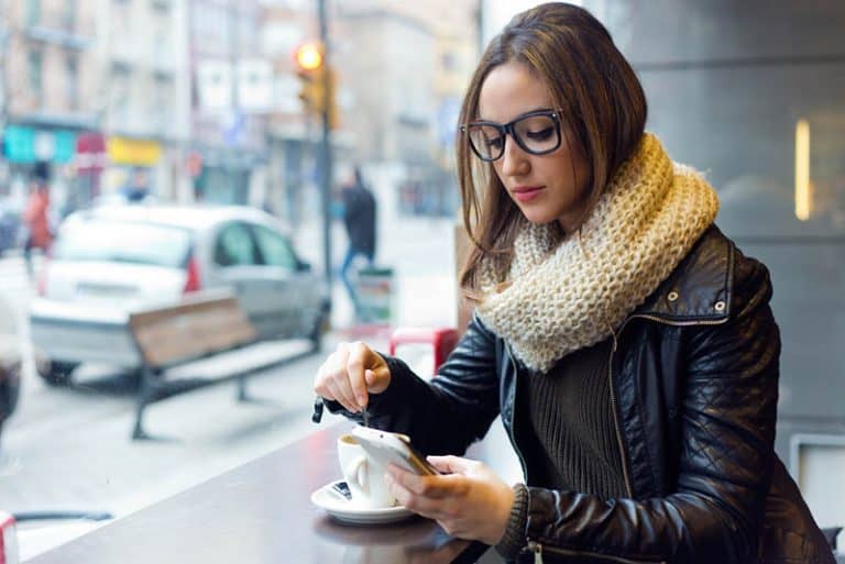 ein Mädchen, das alleine beim Kaffee und einem Schlüssel auf ihrem Handy sitzt