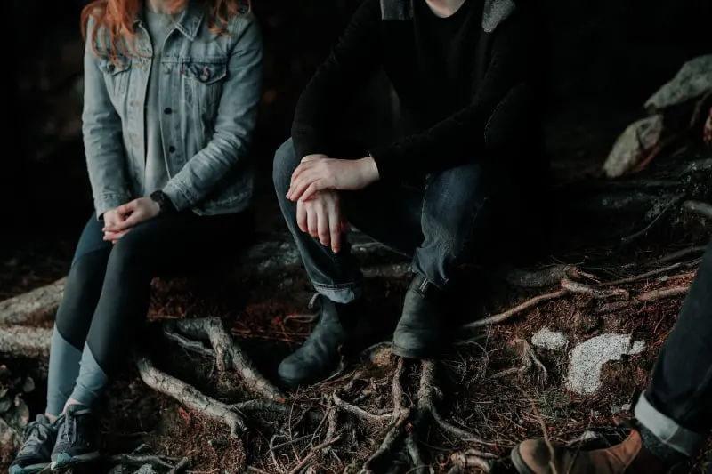 zwei Personen sitzen auf Holzplatte