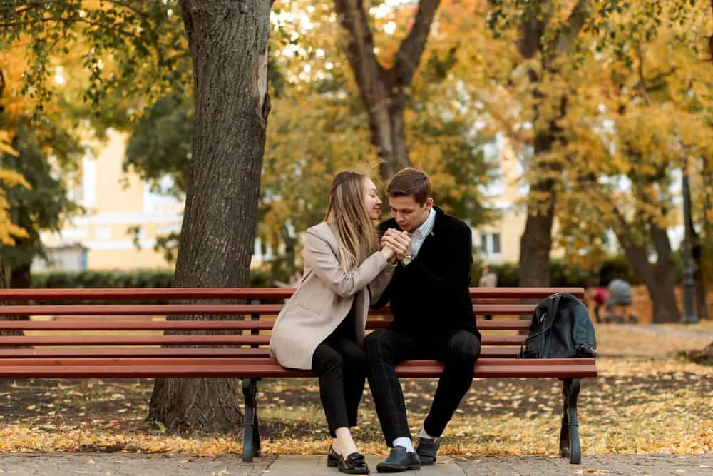 Auf einer Parkbank küsst ein Mann die Hände einer lächelnden Frau