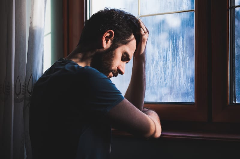 Ein junger trauriger Mann steht am Fenster