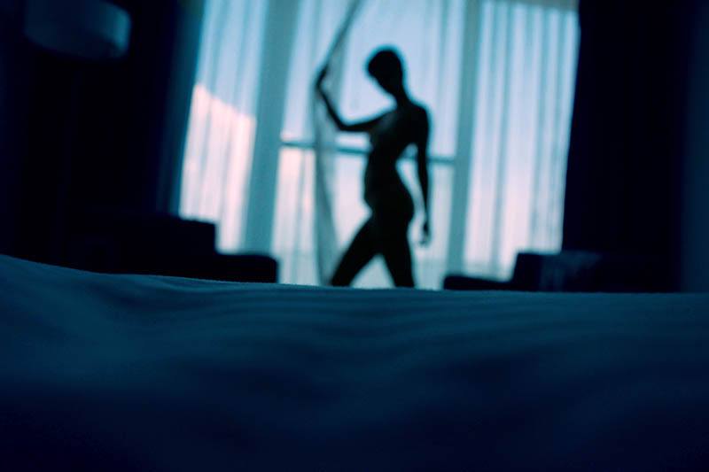 Eine hübsche Frau steht am Fenster in einem dunklen Schlafzimmer
