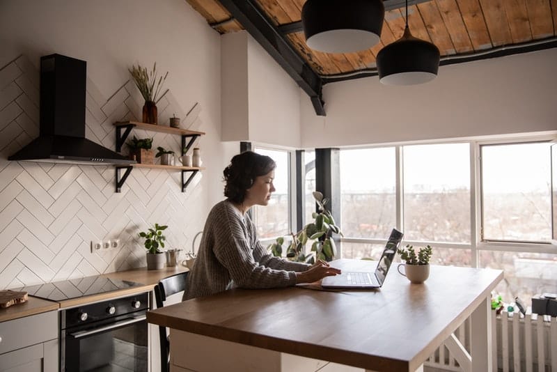 Frau in der Küche sitzt und knöpft auf Laptop