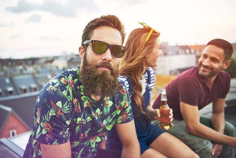 Mann mit Bart und Sonnenbrille schaut in die Kamera, während zwei Freunde hinter ihm sind