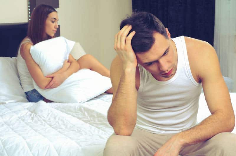 Verärgerter Mann, der Probleme hat, mit seiner Freundin auf dem Bett zu sitzen